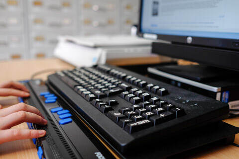 Persoon gebruikt een braillelezer bij een computerscherm