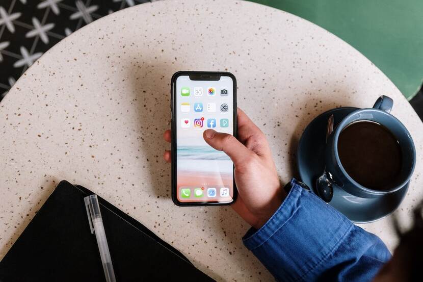 Foto van een hand die een zwarte Iphone vast heeft. Op de Iphone zijn icoontjes van verschillende apps te zien.