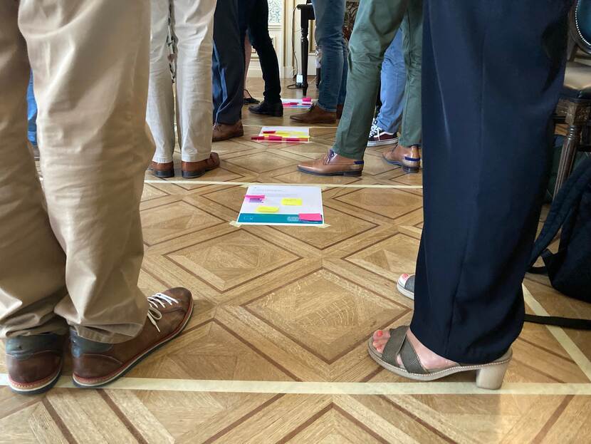 Deelnemers van de werksessie zijn interactief bezig met het frame van informatiehoudingen groot op de vloer geplakt.