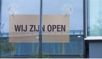 Een bordje met de tekst "Wij zijn open" hangt voor een raam